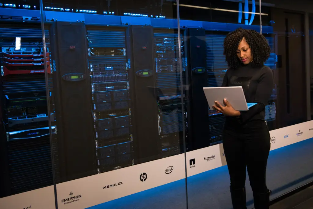 woman on a laptop standing next to servers in a datacenter